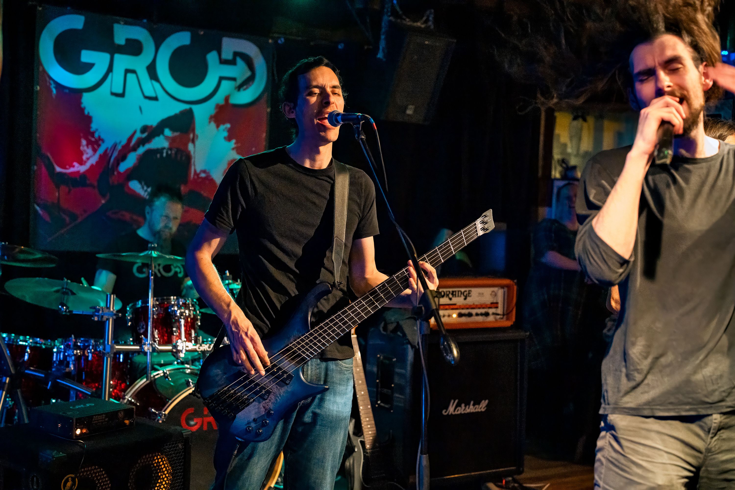 Alex Carol singing and playing bass live on stage.